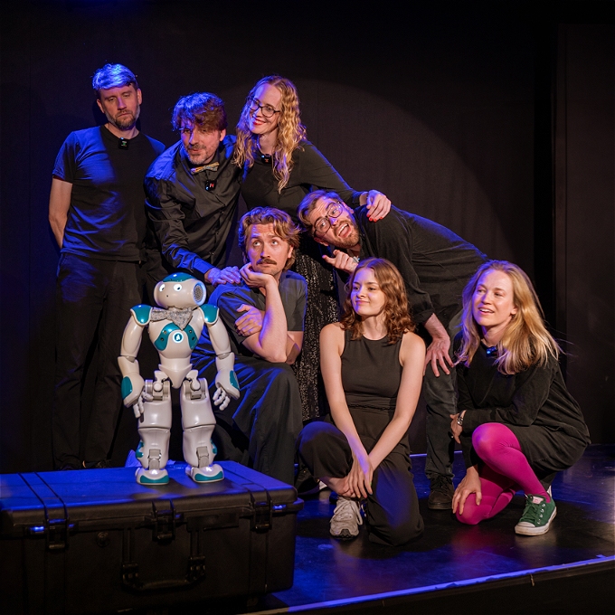 Cast of human theatre actors from Improbotics, looking lovingly at a cute small humanoid robot