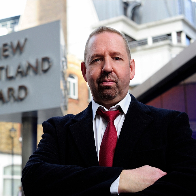 Cop-turmed comedian Alfie Moore stood with arms folder in front of Scotland Yard sign