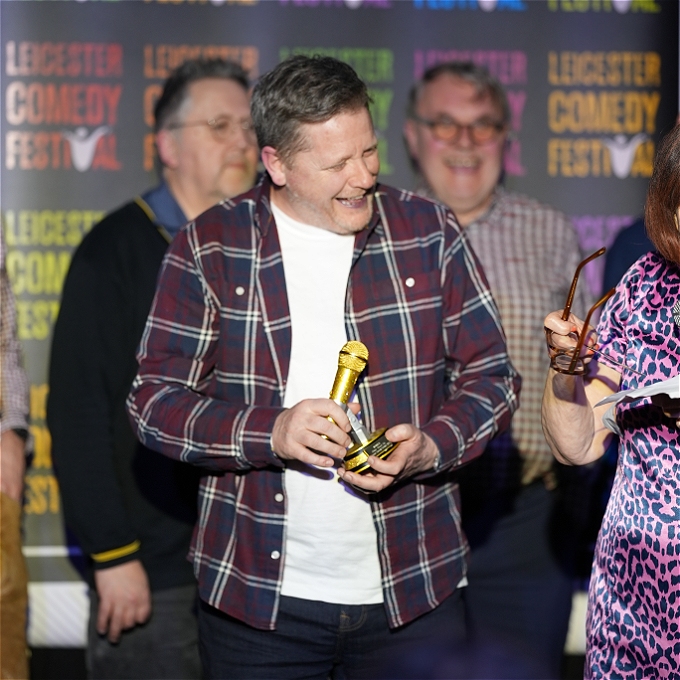 A smiling Kevin Daniel holding the winner's trophy at the 2024 Silver Stand Up competition.