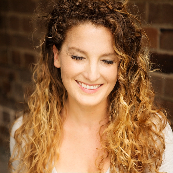 Female comedian with brown and blonde curly hair smiling